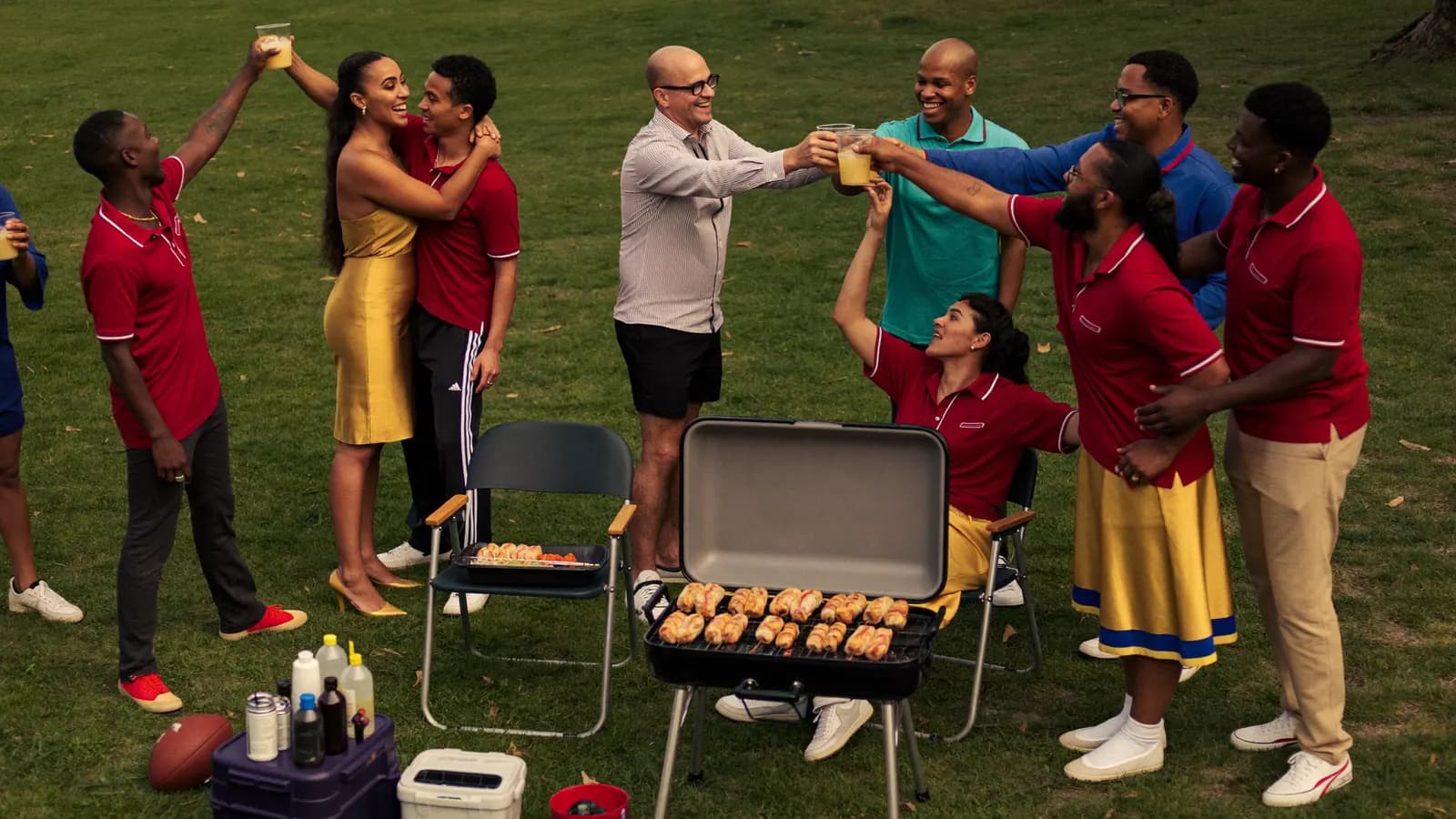 An alumni reunion tailgate: old friends in matching colors raising a toast around the grill on a campus lawn